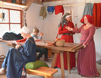 Fire mennesker klædt i middelaldertøj samlet omkring et bord